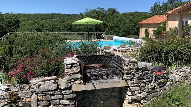 A stone wall with a grill, a swimming pool, and a green umbrella in a lush, green landscape. - House / Villa - Saint Chels (Saint-Chels)