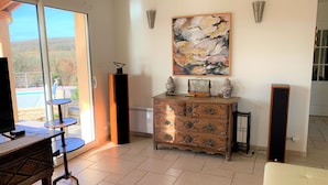 A room with a large window, a wooden dresser, a painting on the wall, and a television on a stand. - House / Villa - Saint Chels (Saint-Chels)