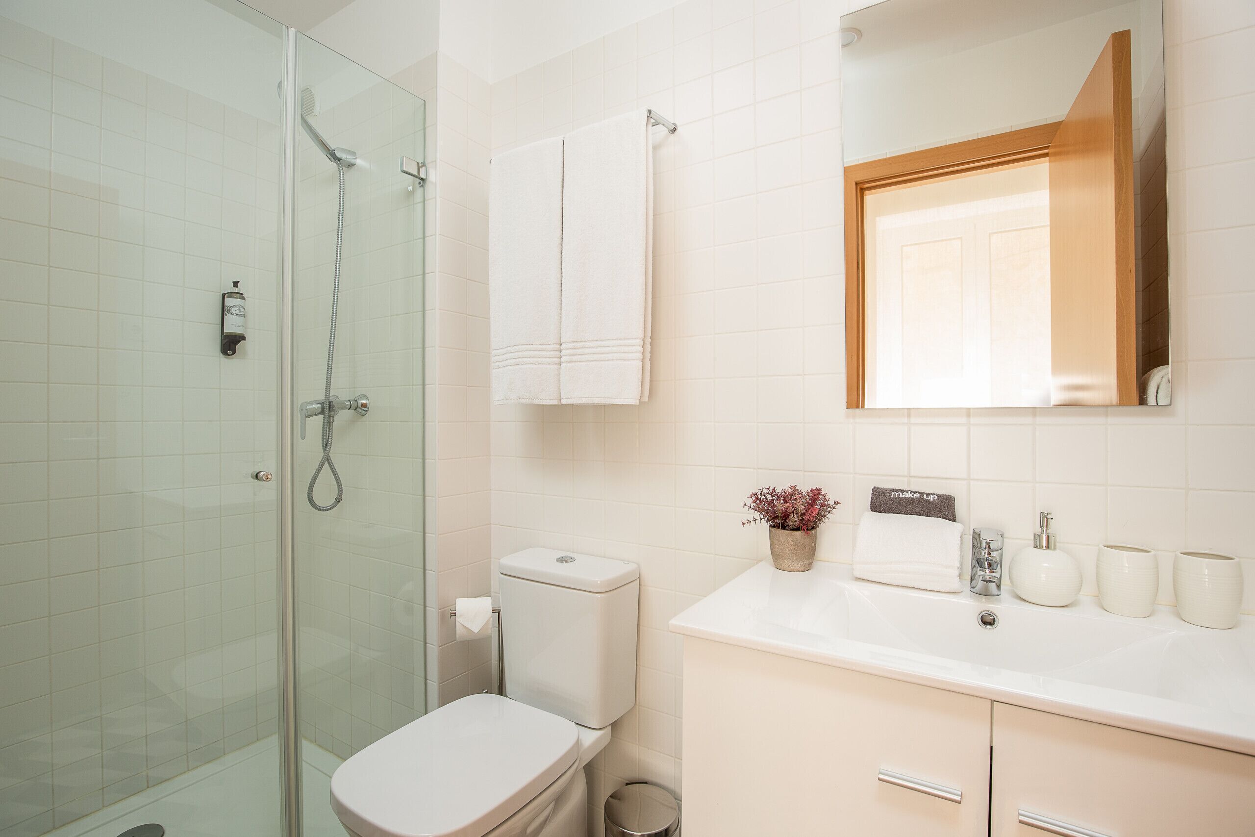 Ein modernes Badezimmer mit Duschkabine aus Glas, Toilette, Waschbecken mit Spiegel und einer kleinen Topfpflanze.