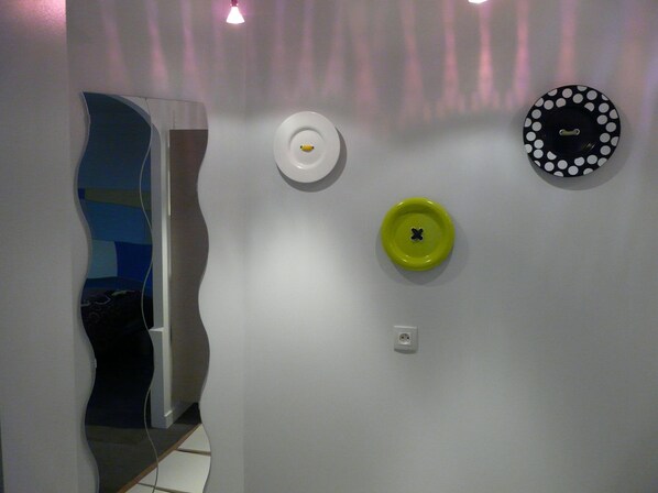 A hallway with a white wall, a door with a blue and white abstract design, and three wall-mounted plates in different colors and patterns.