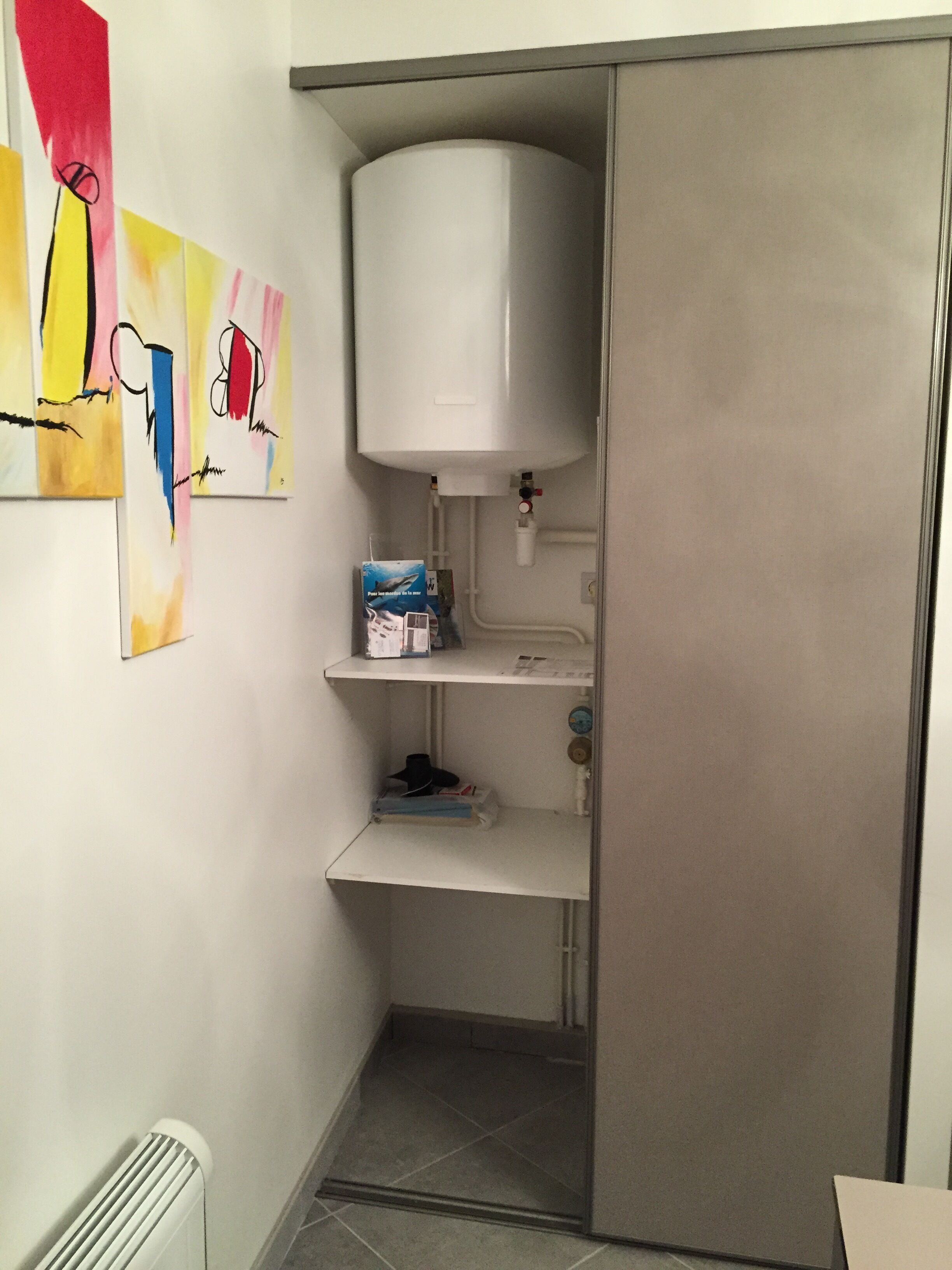 A bathroom with a white toilet, a towel rack, a shelf with toiletries, and a radiator.