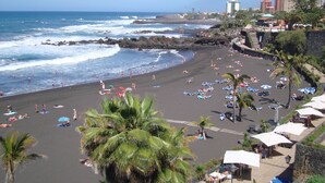 A beach with umbrellas and lounge chairs, a rocky shoreline, and buildings in the background.