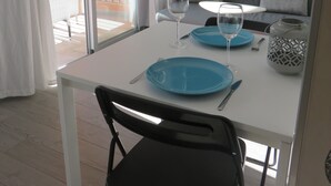 A dining area with a table set for two, a sofa, and a view of an outdoor balcony.