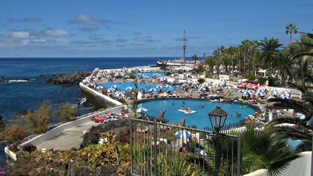 A coastal resort with multiple swimming pools, a rocky shoreline, and palm trees.