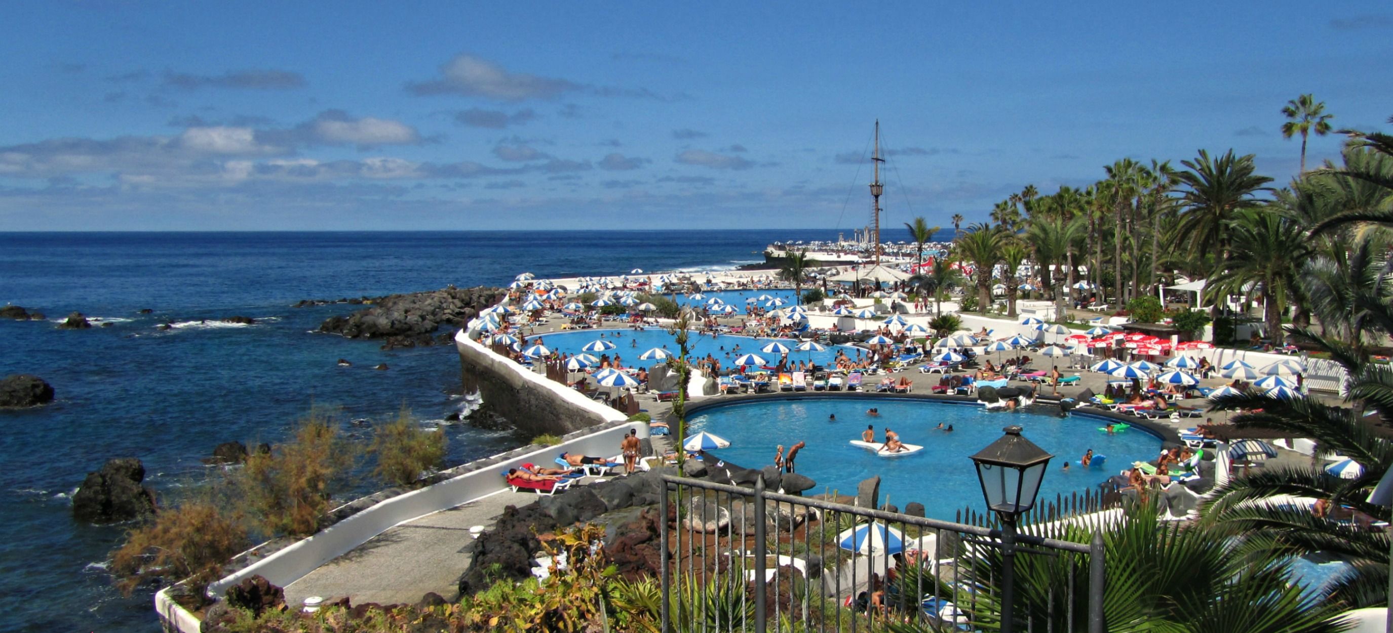 Ein Küstenresort mit mehreren Schwimmbecken, einer felsigen Küstenlinie und Palmen.