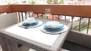 A wicker table set with plates, bowls, and wine glasses on a balcony overlooking a cityscape with buildings and palm trees.