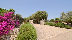 A paved pathway leading to a stone gate, surrounded by well-maintained hedges and flowering plants.