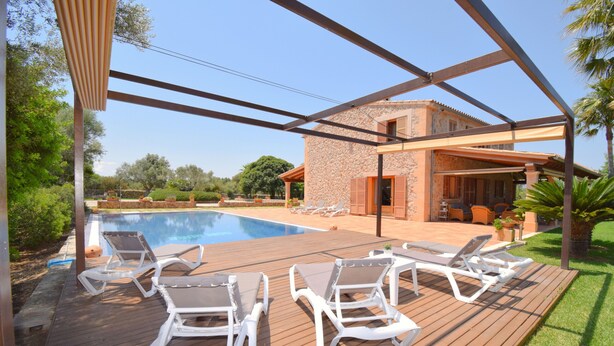 A poolside area with lounge chairs, a wooden deck, and a stone building in the background.
