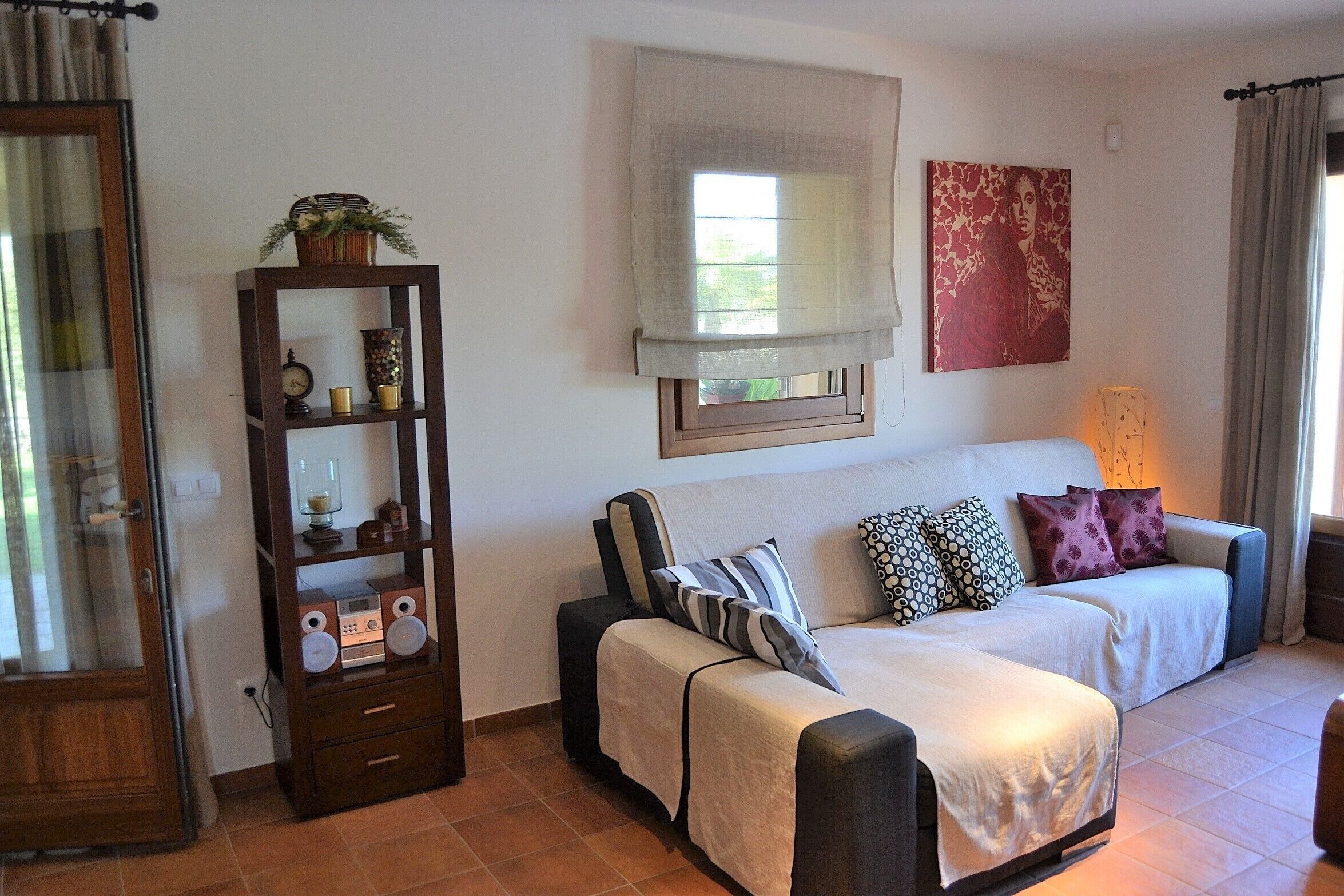 A cozy living room with a sofa set, a wooden side table with decorative items, and a window with a view.