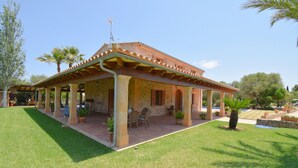 A house with a covered patio, a pool, and a well-maintained lawn.