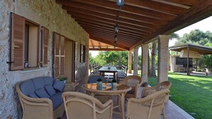 A covered outdoor seating area with wicker furniture, a table, and a pergola with wooden beams.