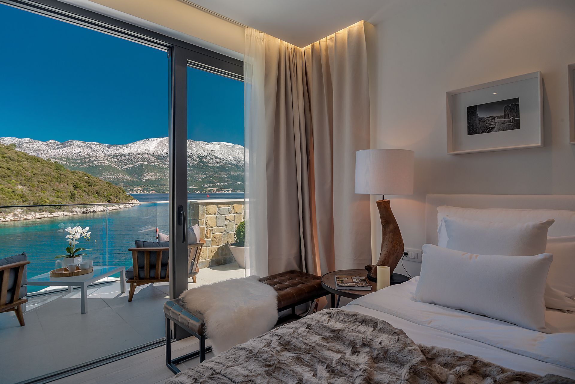 A hotel room with a large window offering a view of a coastal landscape.