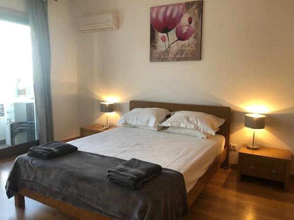 A neatly made bed with white linens and a dark gray blanket, flanked by two bedside lamps on wooden nightstands. - Ground floor apartment with Pool, Central Location (Tavira)