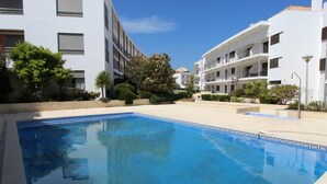 Una piscina rodeada de edificios blancos con balcones, y abundante vegetación.