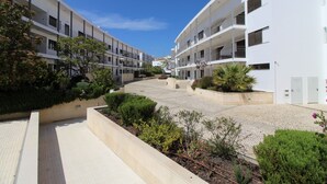 Un edificio de apartamentos moderno con varios balcones, un patio empedrado y zonas ajardinadas con diversas plantas.