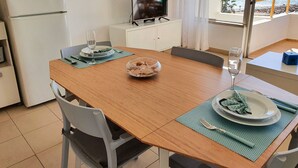 A dining area with a wooden table, chairs, a bowl of snacks, and a TV on a cabinet.