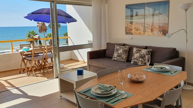 A balcony with a dining table, chairs, a sofa, and a large window overlooking the sea.