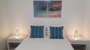 A bed with two pillows, two bedside tables with lamps, and a wall with a painting of a beach scene.