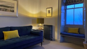A living room with a blue sofa, a radiator, a lamp, and a window with a view.