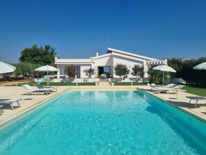 A modern house with a swimming pool, sun loungers, and umbrellas.