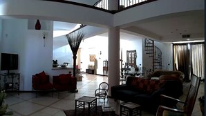 A spacious living area with a high ceiling, a TV mounted on a stand, and a staircase leading to an upper level. - "House Sbrizza" in the countryside 15 minutes from the sea (Rosolini)