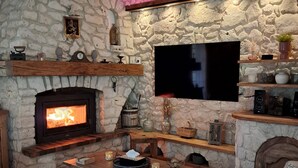 A cozy living room with a stone fireplace, wooden furniture, and a flat-screen TV mounted on the wall.