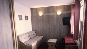 A small, cozy room with a sofa, a small table, and a bench. There are two wall-mounted lights and a television on the wall. - Nice renovated apartment ** Terrace, skiing, parking, shops at 30m (La Plagne Tarentaise)