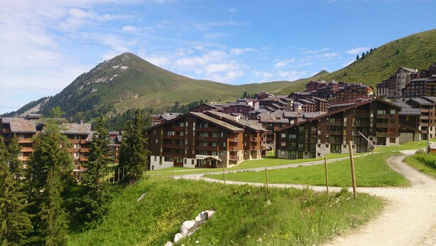A mountain resort with wooden buildings, a dirt path, and a mountain in the background. - Nice renovated apartment ** Terrace, skiing, parking, shops at 30m (La Plagne Tarentaise)