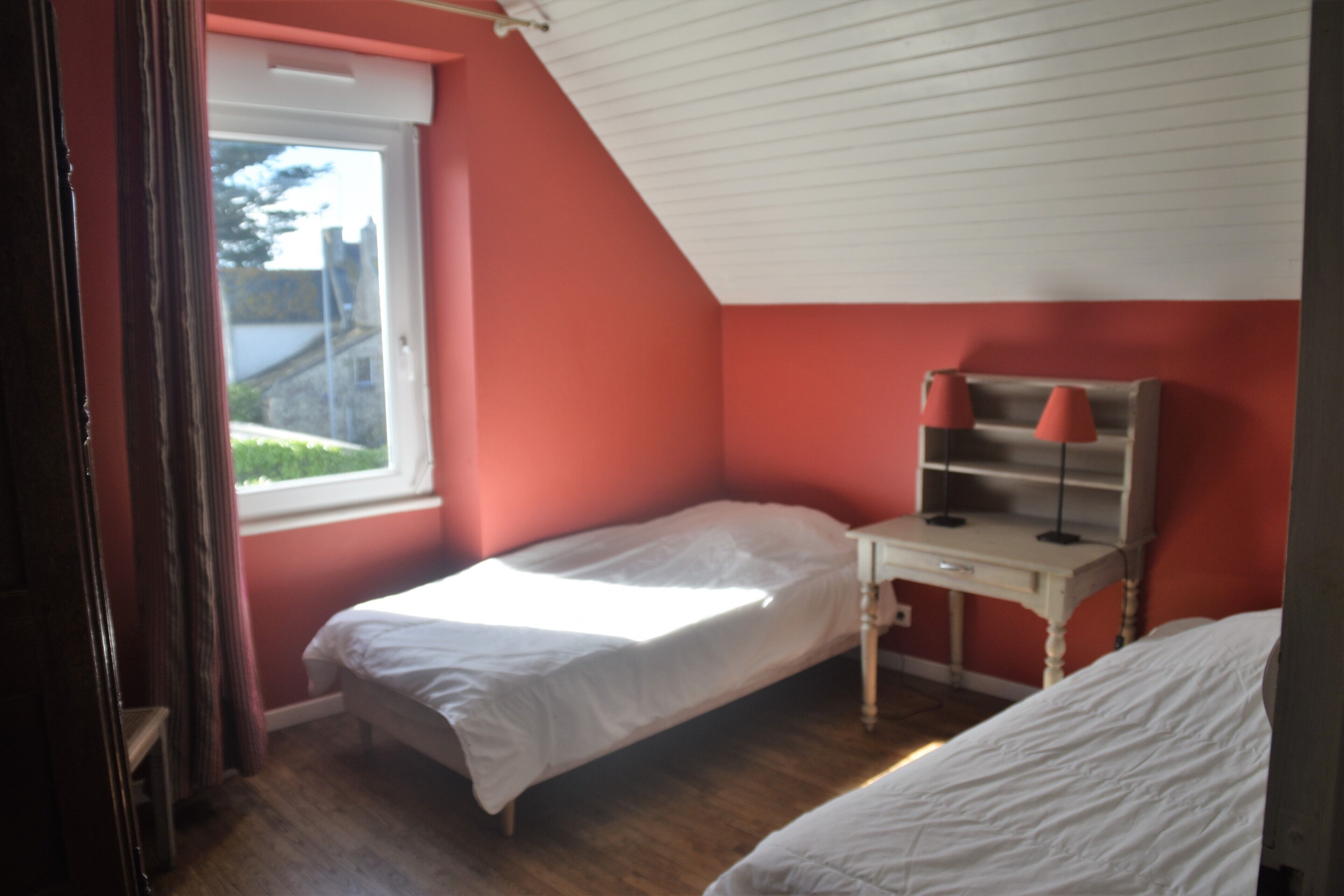 Une chambre avec deux lits simples, une fenêtre et un bureau avec une lampe.