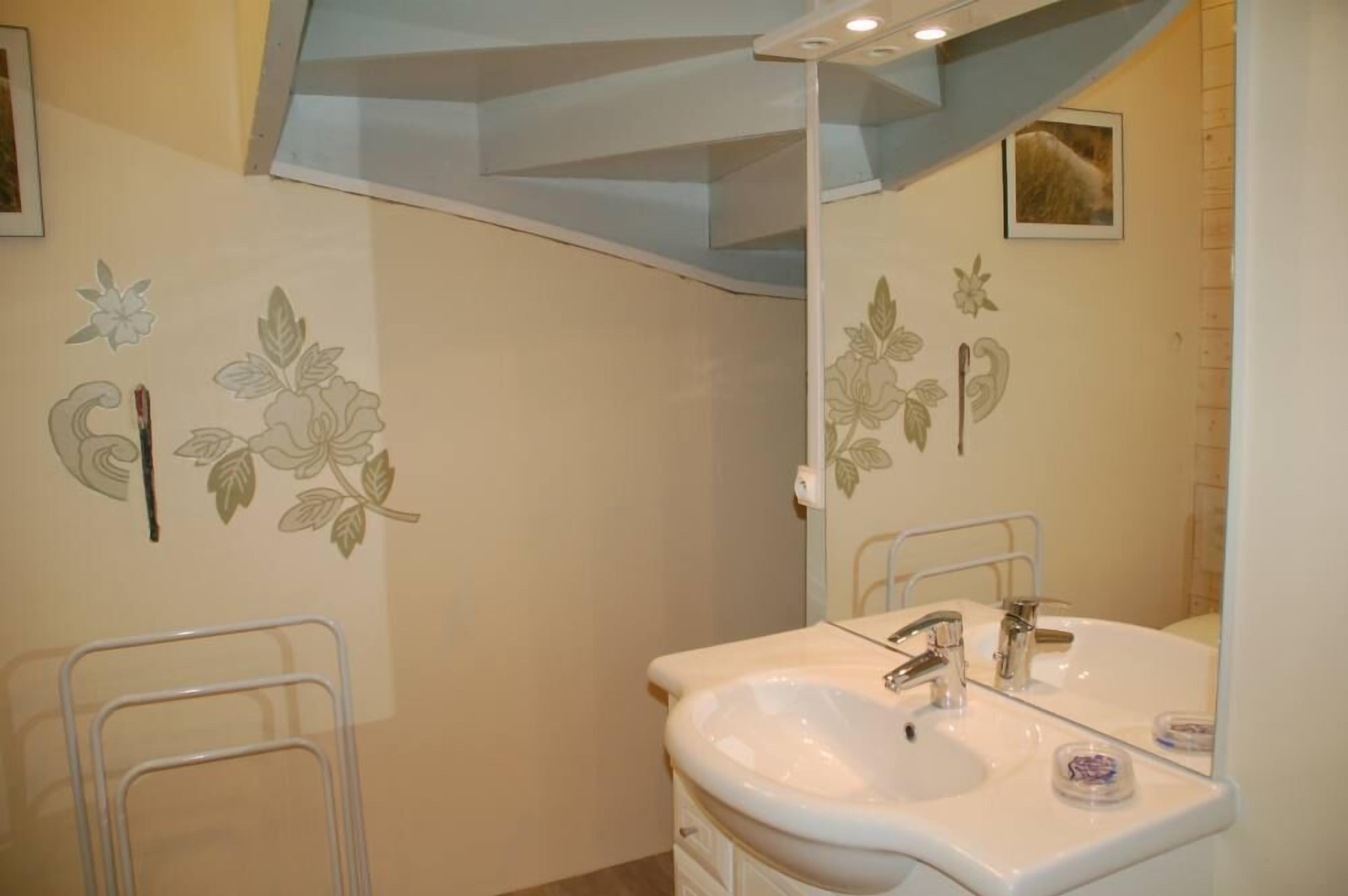 A bathroom with a white sink, mirror, and floral wall decoration.