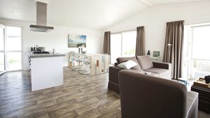 A modern living room with a sofa, a coffee table, and a kitchen area with a bar. - EuroParcs Schoneveld (Breskens)