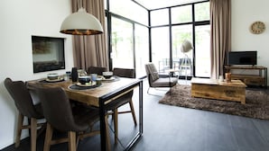 A modern living room with a dining area, large windows, and a television. - EuroParcs Schoneveld (Breskens)