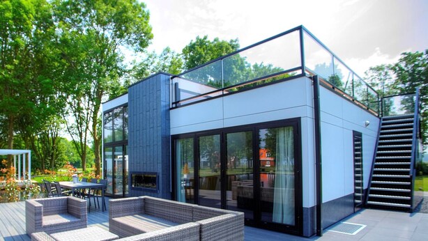 A modern house with a glass facade, outdoor seating, and a wooden deck. - EuroParcs Schoneveld (Breskens)