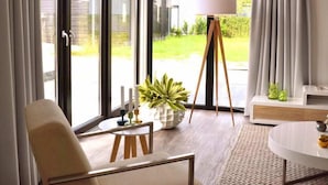 A modern living room with a large window, a floor lamp, a sofa, and a dining table. - EuroParcs Schoneveld (Breskens)