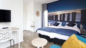 A modern bedroom with a large bed, a desk, and a view of the sea through a window. - EuroParcs Schoneveld (Breskens)