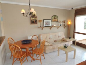 Un'area pranzo con un tavolo rotondo, sedie, una poltrona, un tavolino con un vaso e mensole a parete con elementi decorativi.