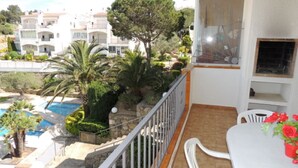 A balcony with a view of a swimming pool, a dining area with a table and chairs, and a small garden with various plants. - JARDINS III 412 Roses (Rosas / Roses)