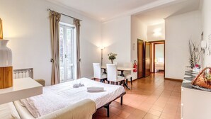 A hotel room with a bed, a desk, a chair, a table with a vase of flowers, and a view of the outside. - Finally In Rome Vatican Apartment - 3 Double Rooms 100MQ (Roma)