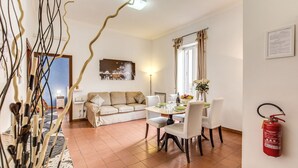 A dining area with a table set for four, a sofa, and a fire extinguisher on the wall. - Finally In Rome Vatican Apartment - 3 Double Rooms 100MQ (Roma)