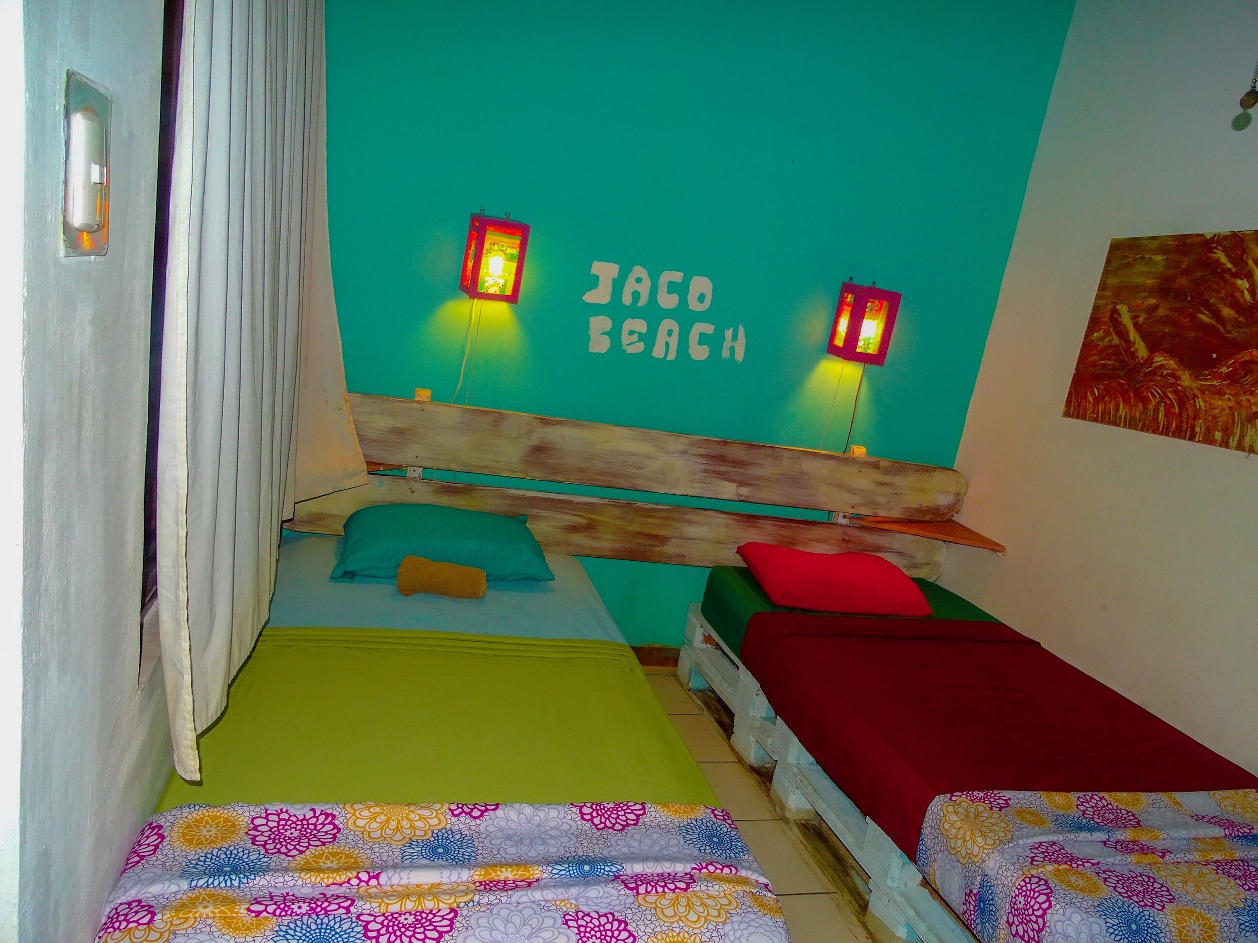 A room with two beds, each with a different colored bedspread. There are two wall-mounted lights and a painting on the wall.