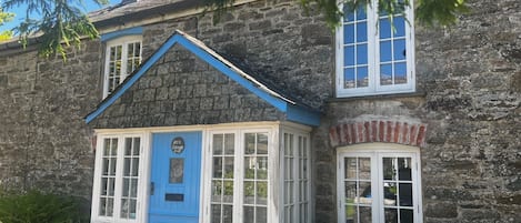A stone cottage with a blue door and white-framed windows.