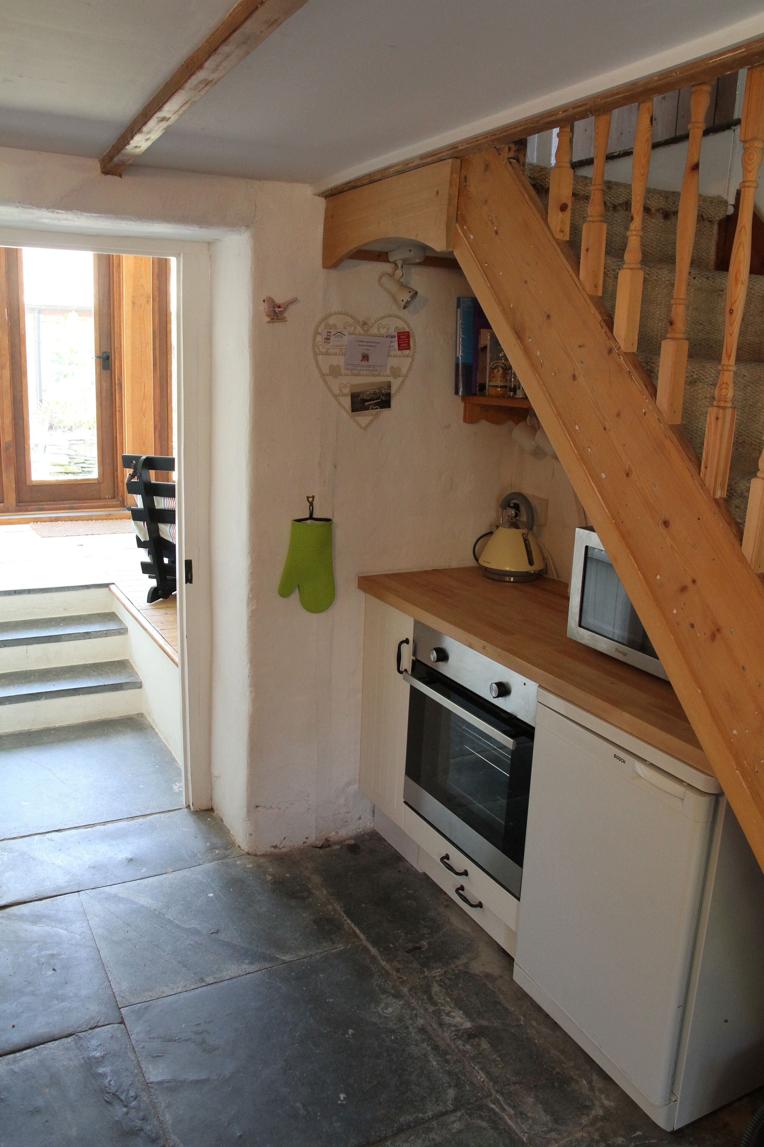 A kitchen with a wooden staircase, a microwave, and a small oven.