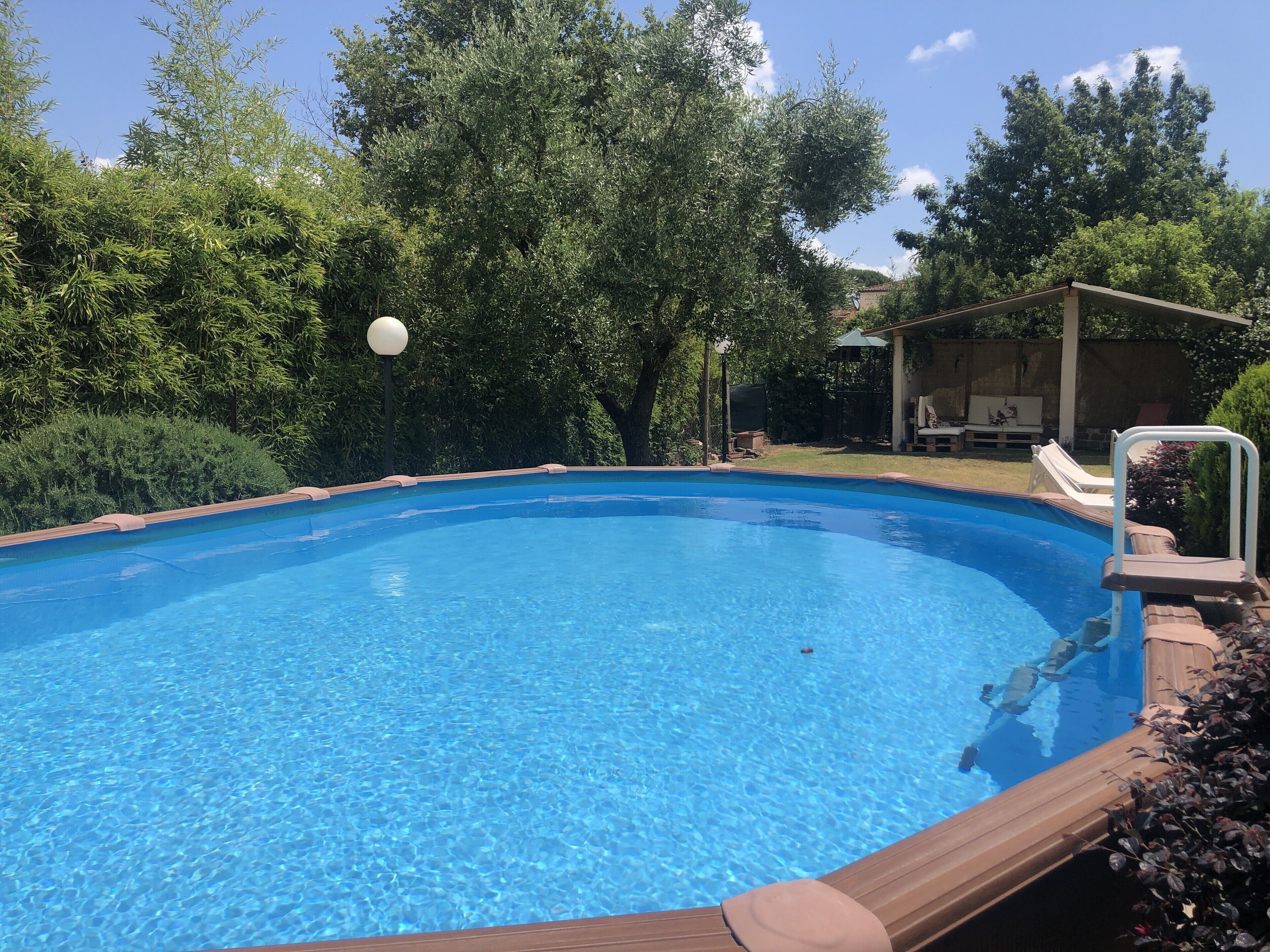 Ein klares, blaues Schwimmbecken, umgeben von üppiger Vegetation und einer überdachten Terrasse.