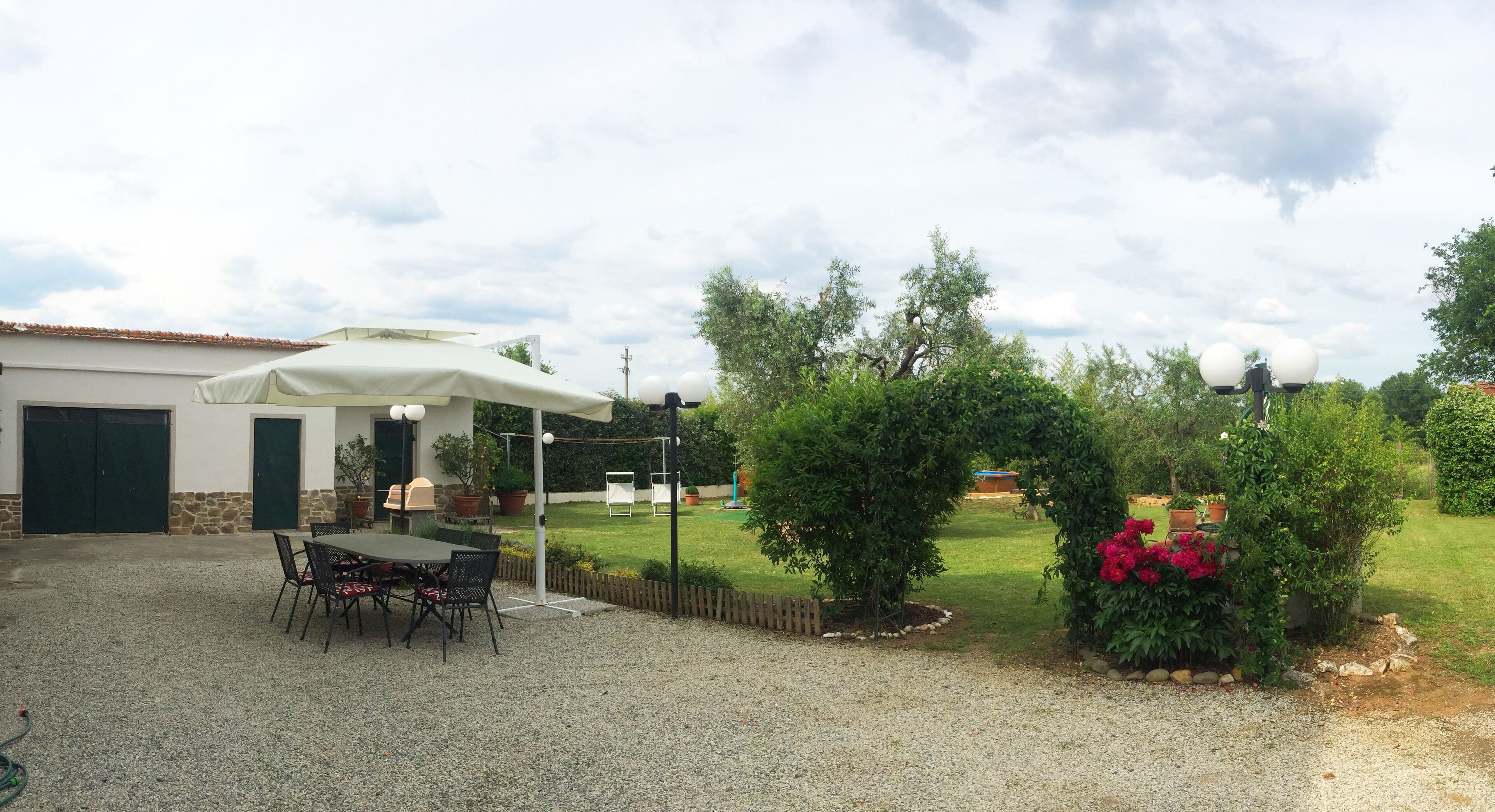 Eine Terrasse mit Tisch und Stühlen, ein überdachter Sitzbereich und ein Garten mit Sträuchern und Blumen.