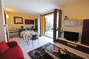 Ein modernes Wohnzimmer mit einer Couch, einem Couchtisch, einem Fernseher und einem Essbereich mit Tisch für zwei Personen.