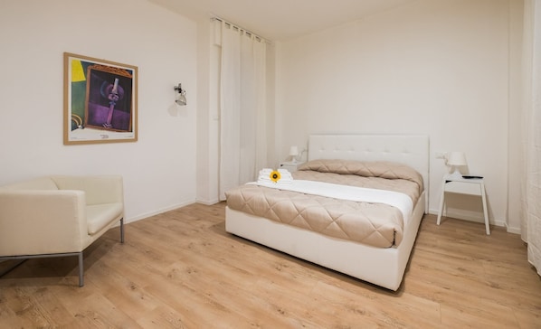 Un dormitorio con cama, una silla, una mesita de noche y un cuadro en la pared.