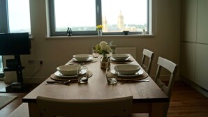 A dining table set with plates, glasses, and cutlery, positioned near a window with a view of a building. - NEW! Luxury Apartment in Truro Centre With Cathedral Views! (Truro)