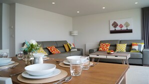 A modern living room with a dining area, grey sofas, colorful cushions, a vase with flowers, and a painting on the wall. - NEW! Luxury Apartment in Truro Centre With Cathedral Views! (Truro)