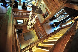 A high-ceilinged wooden interior with a central staircase, a television, and a hanging light fixture.