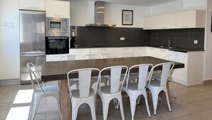 Une cuisine moderne avec des meubles blancs, un îlot central doté de chaises, des appareils électroménagers intégrés et des spots encastrés au plafond.